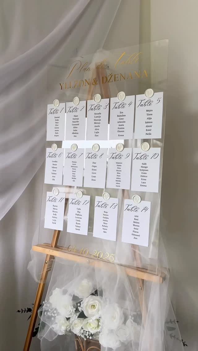 Acrylic seating chart on a wooden easel with white guest lists and white roses.