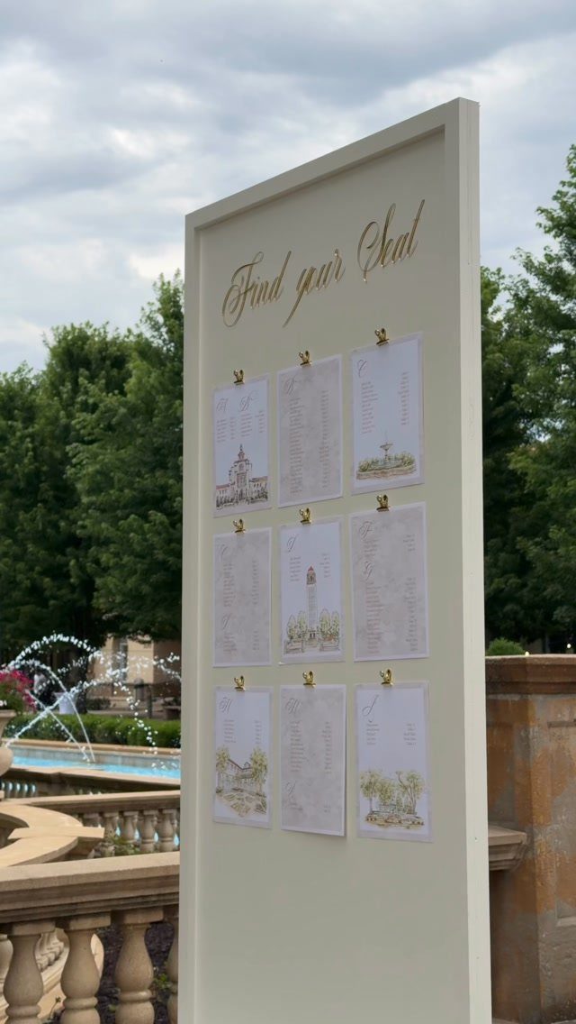 White seating chart board with gold lettering and clipped lists of guest names.