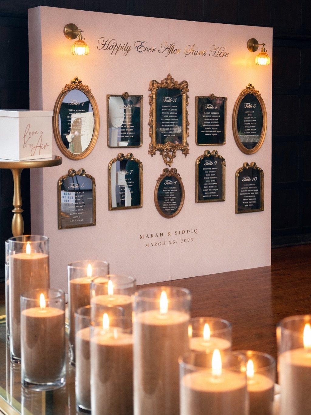 Ornate gold-framed mirrors used as a wedding seating chart on a pink wall.