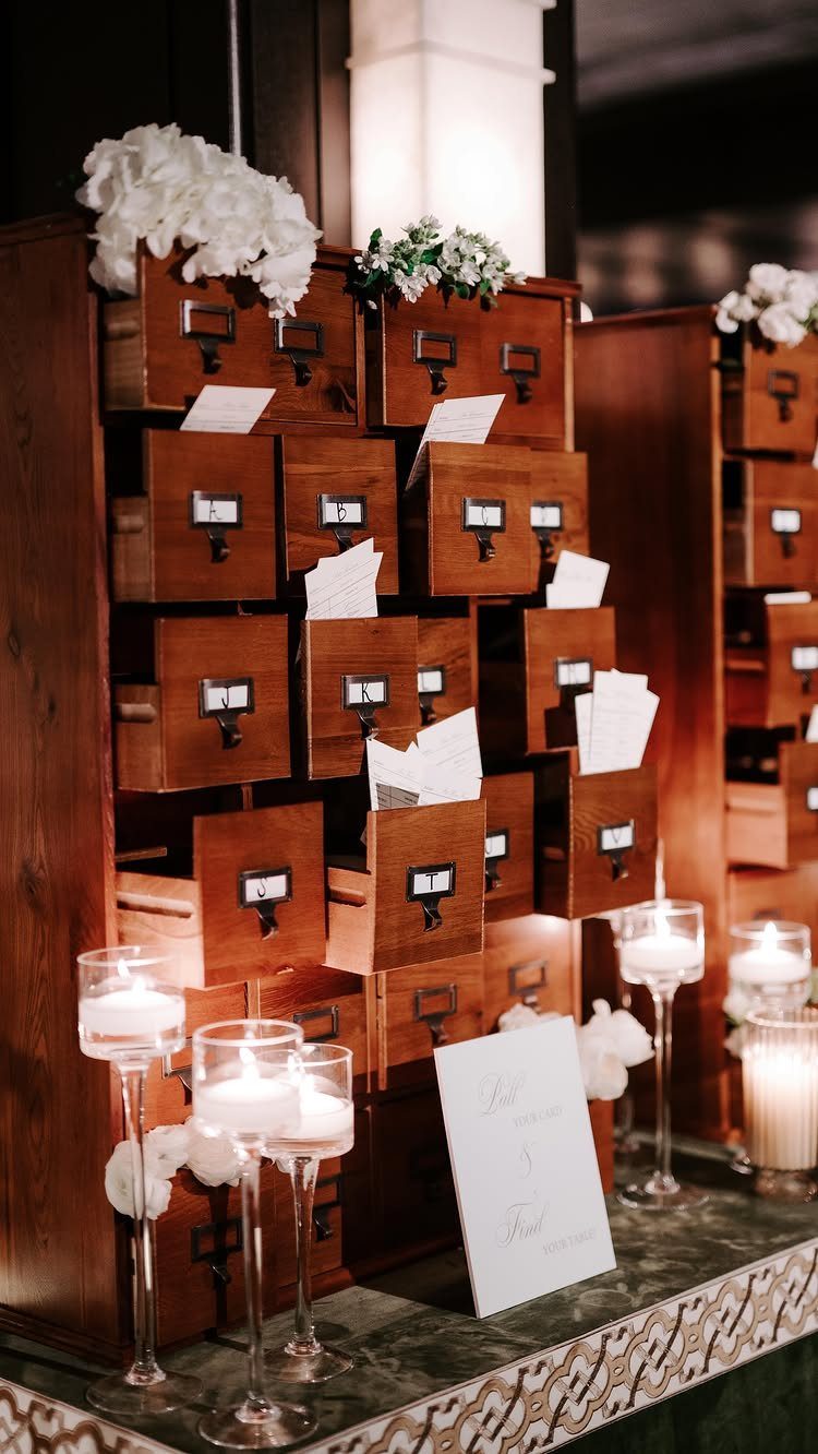 Vintage wooden library card catalog used as a wedding seating chart with candles.