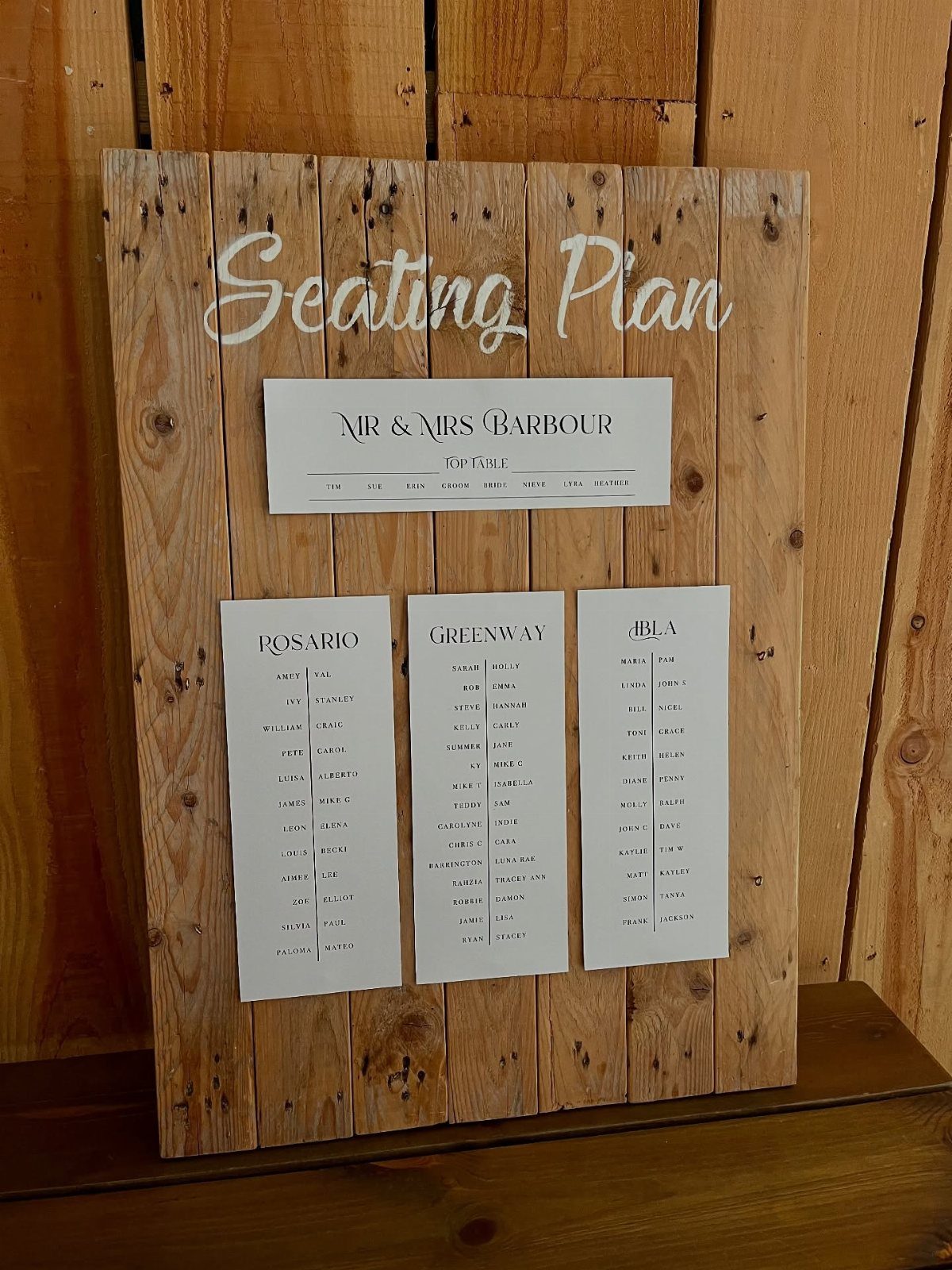 Rustic wooden pallet seating plan with white guest lists and cursive lettering.