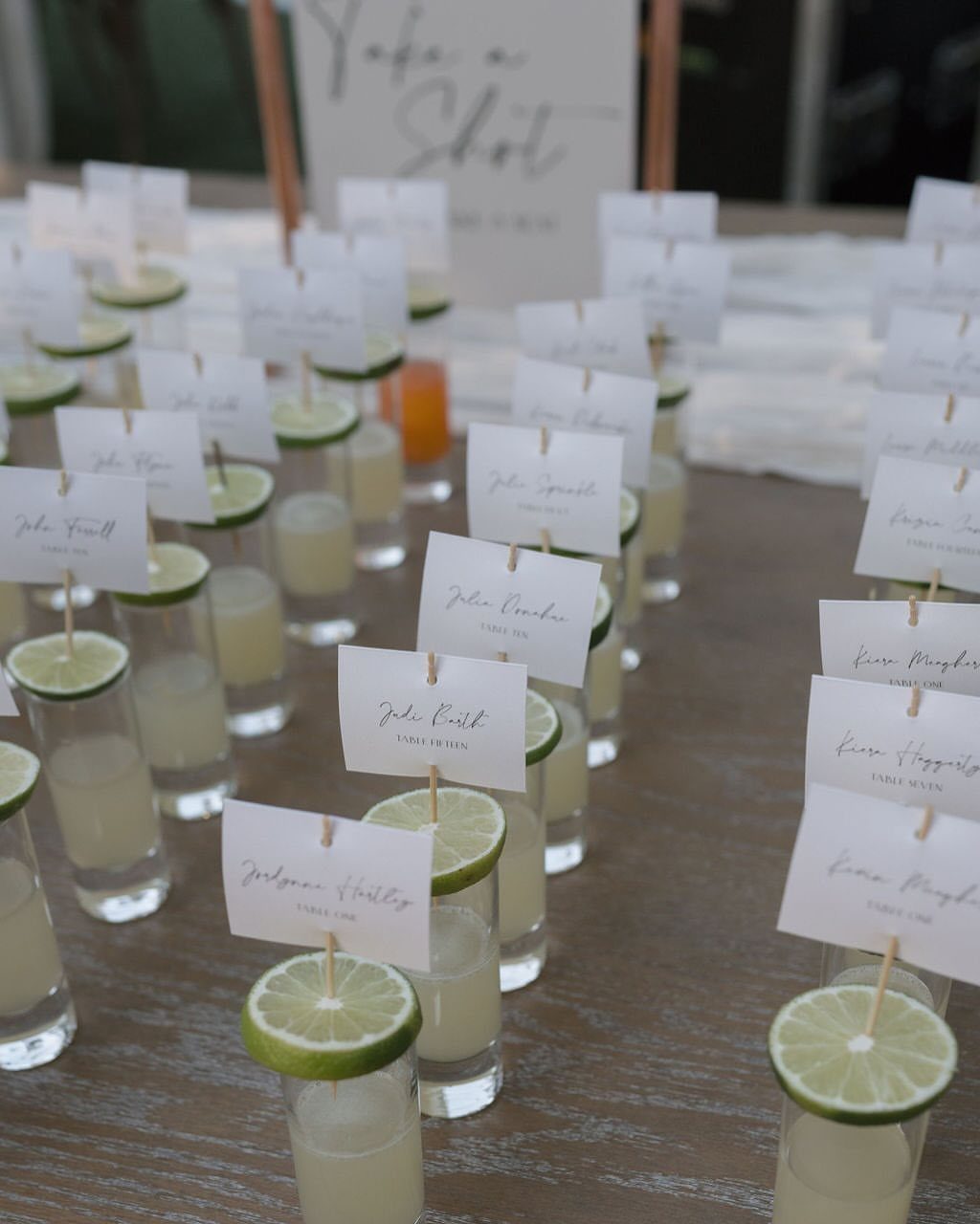 Shot glasses with lime slices and name cards arranged on a wooden table.