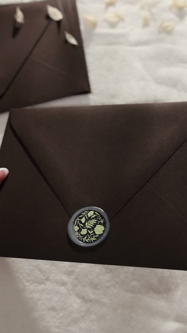 Dark brown envelopes with a grey floral wax seal on white fabric.
