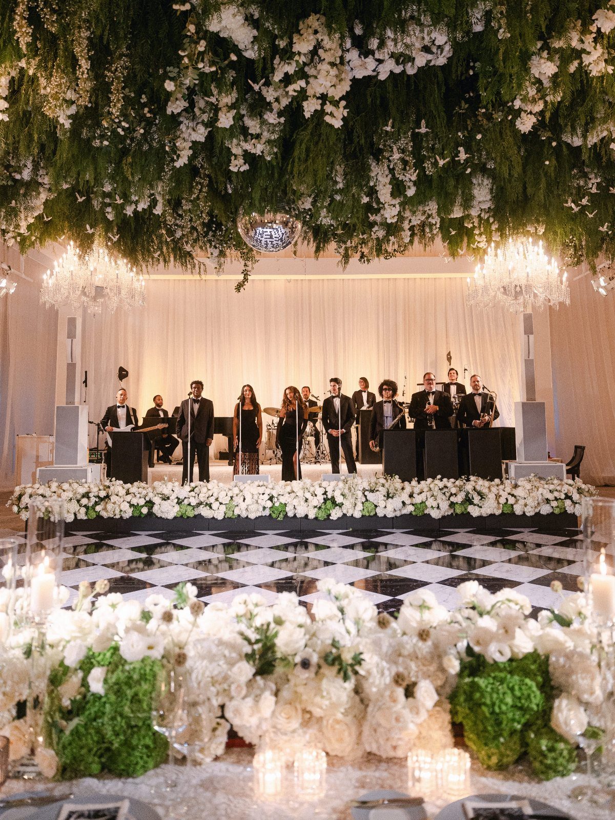 Live band performing on stage above a checkered dance floor with floral decor