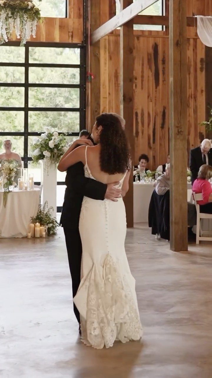 Bride in white gown dancing with her father in a rustic wooden barn