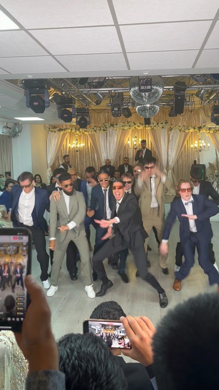 Men in suits and sunglasses dancing energetically on a wedding reception dance floor
