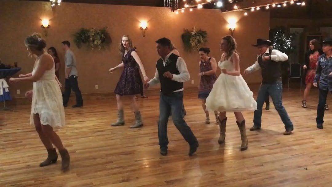 Wedding guests and a bride in cowboy boots dancing on a wooden floor