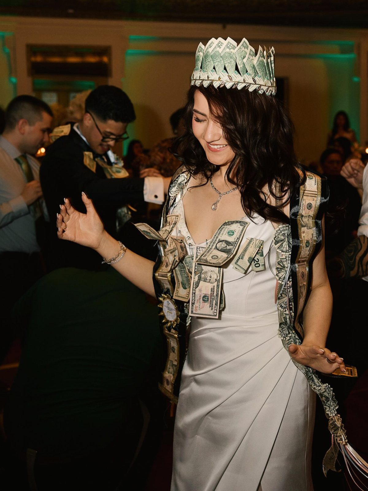 Bride wearing a crown and sash of money while dancing at her wedding reception