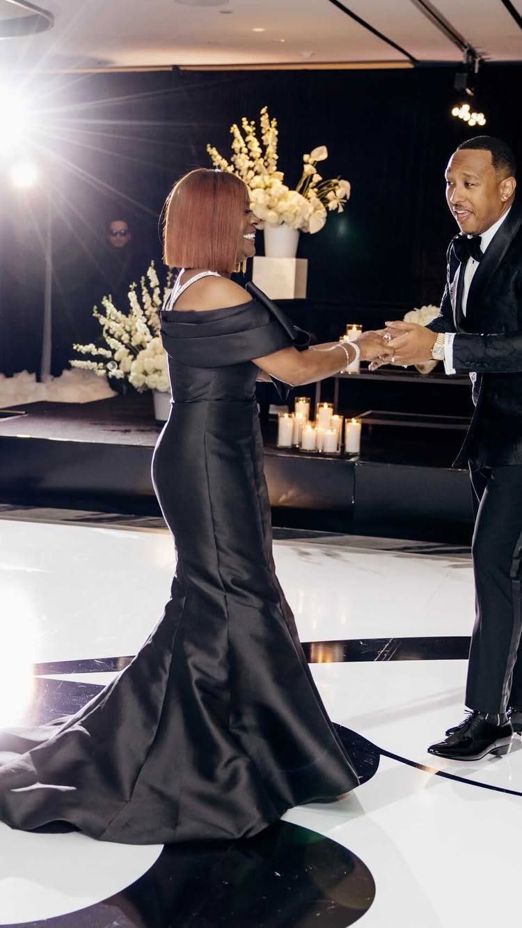 Man in tuxedo and woman in black gown dancing on white dance floor