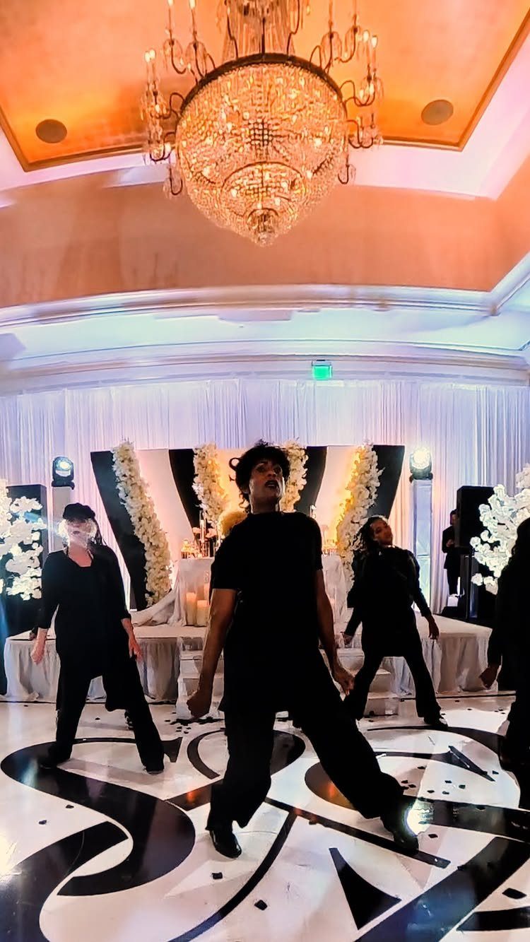 Dancers in black outfits performing on a patterned dance floor under a chandelier