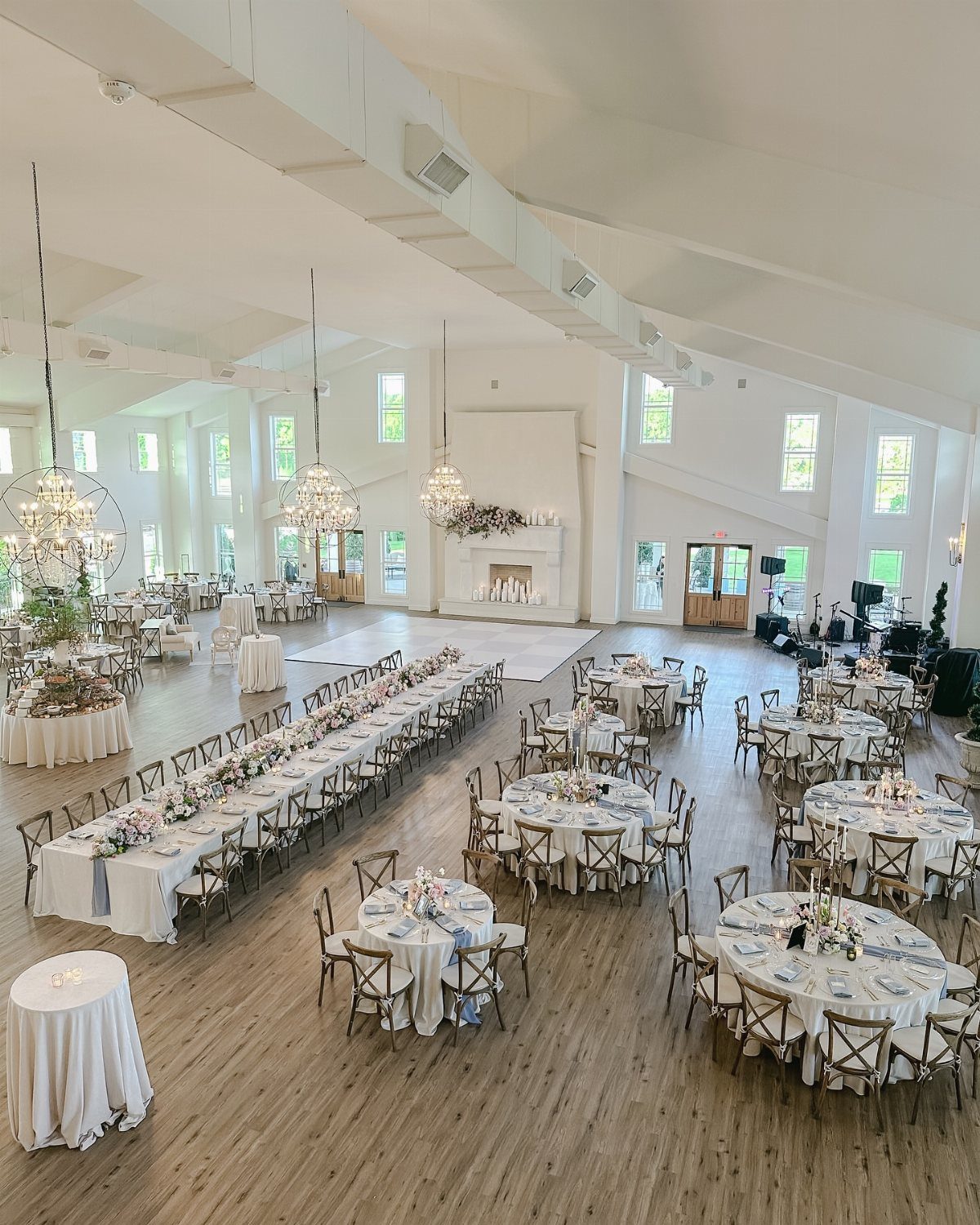 Wedding reception hall with a mix of round and long tables, white linens, and chandeliers.