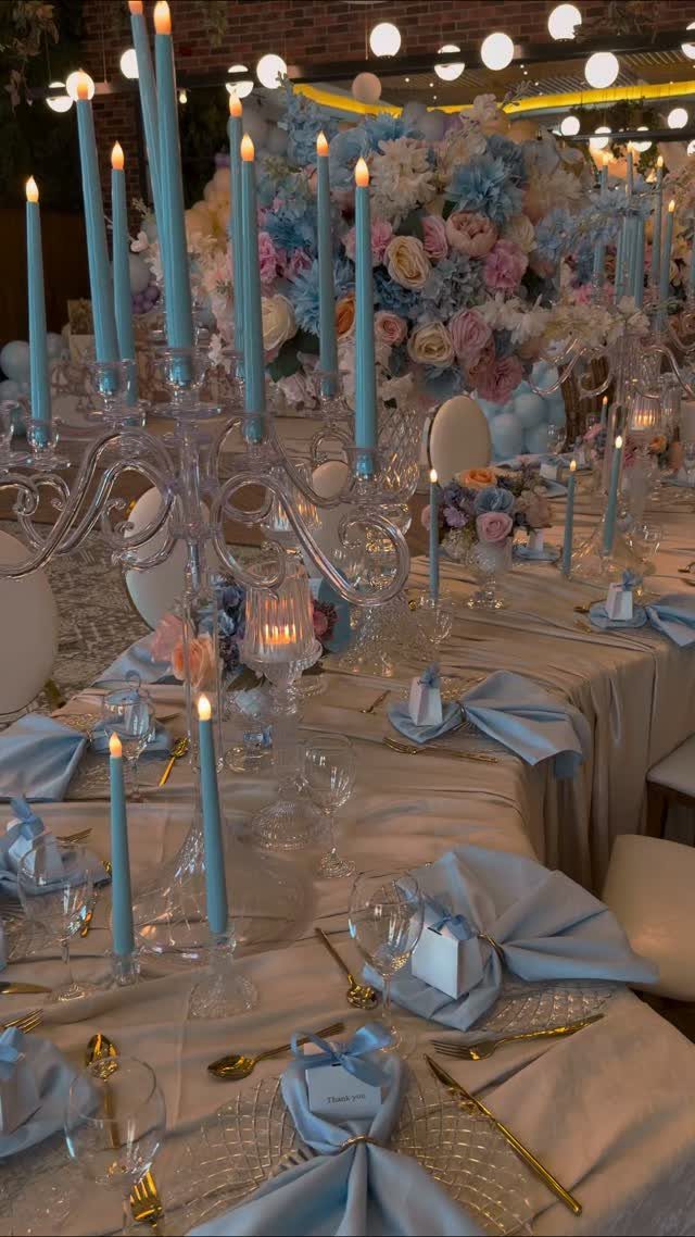 Wedding table setting with blue candles, blue napkins, and large floral centerpieces.