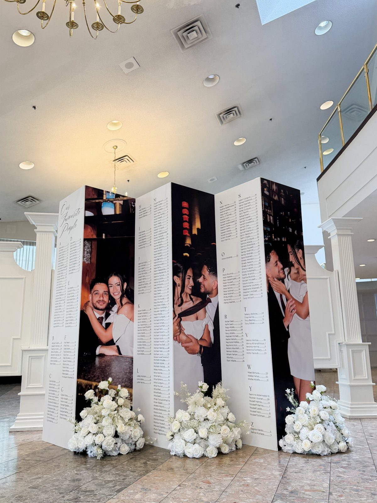 Three-panel wedding seating chart with couple photos and white floral arrangements at base