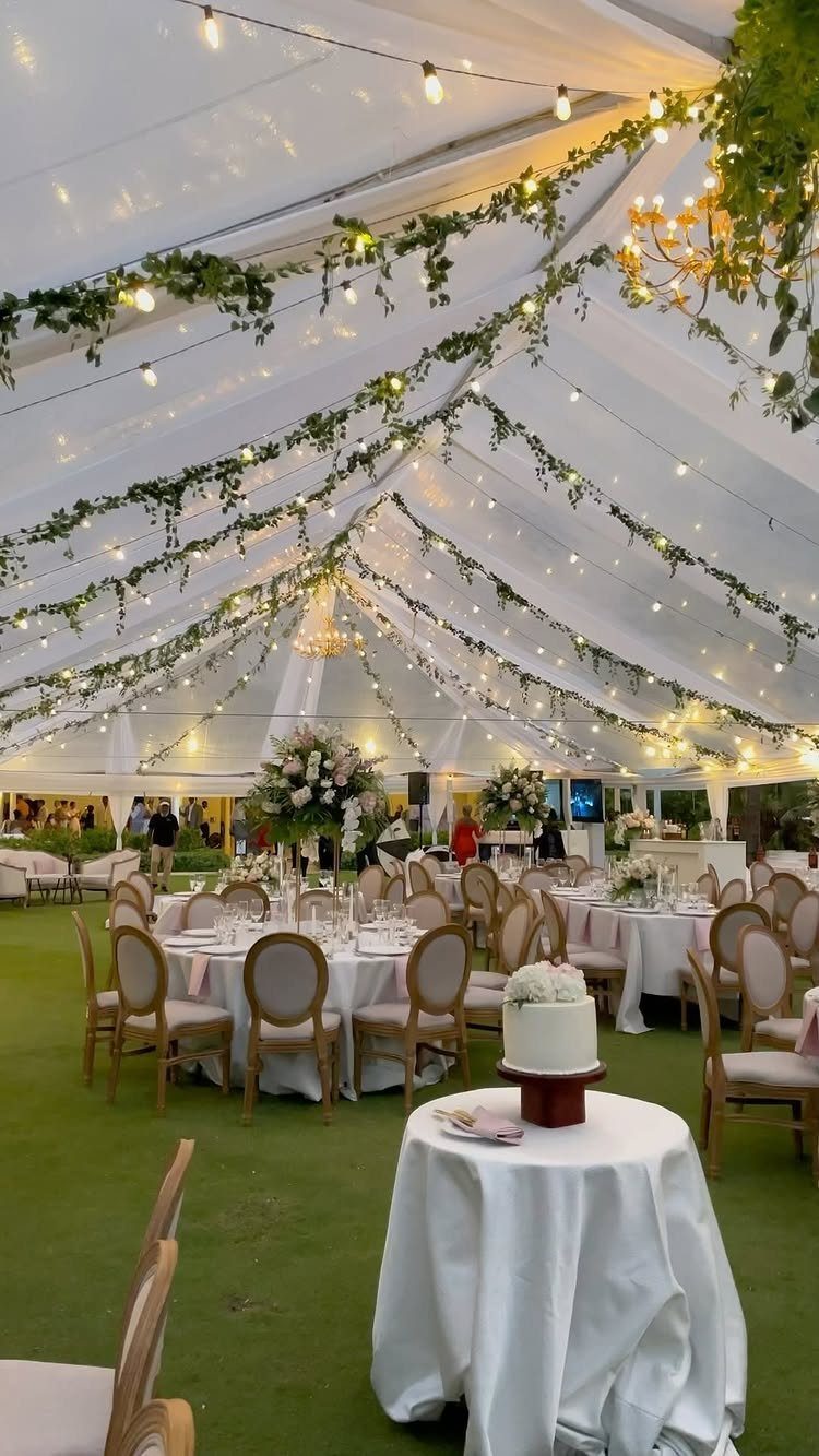 Wedding reception inside a white tent with round tables, greenery, and string lights.
