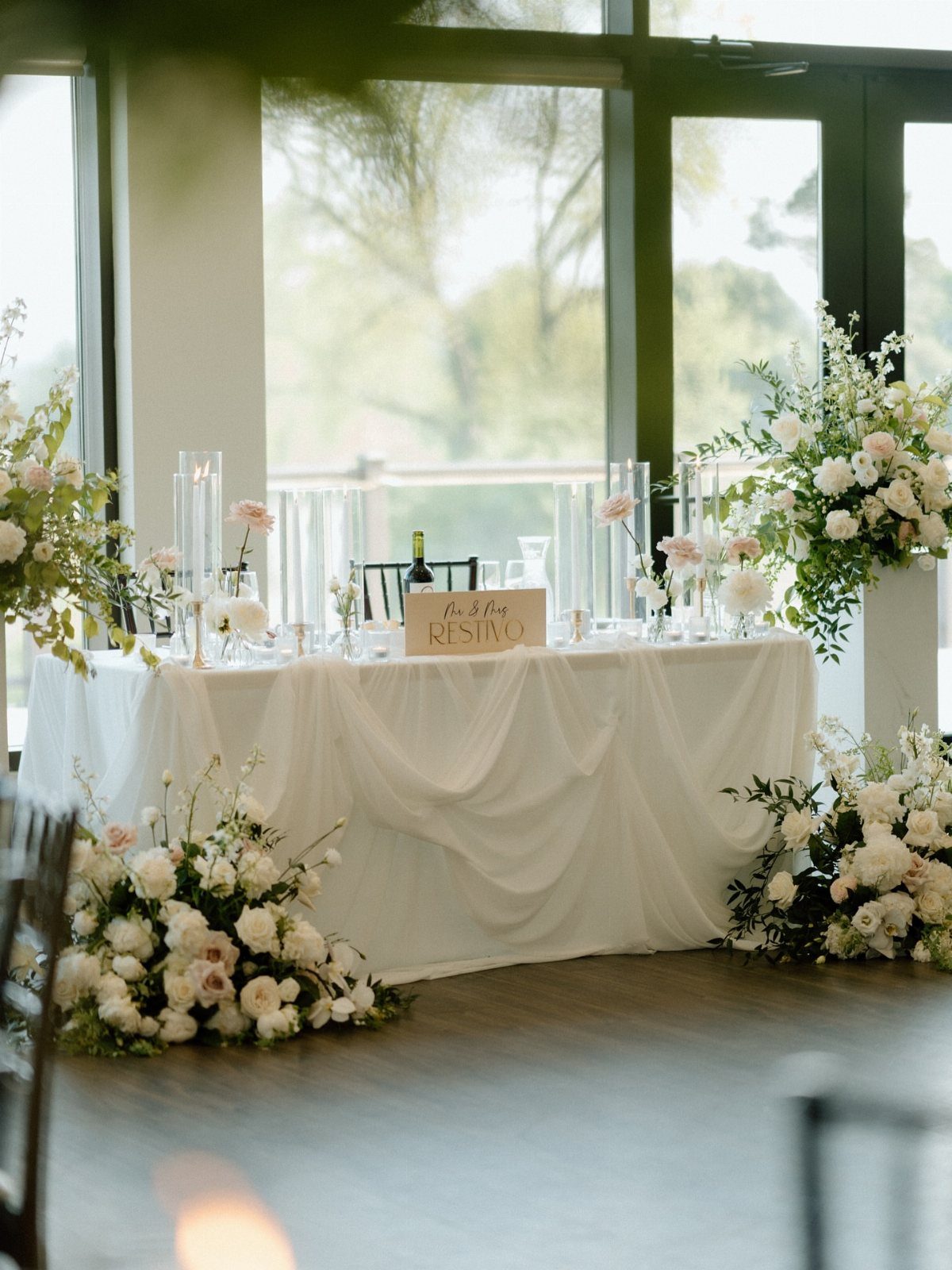 White draped wedding head table decorated with lush white and blush floral arrangements.