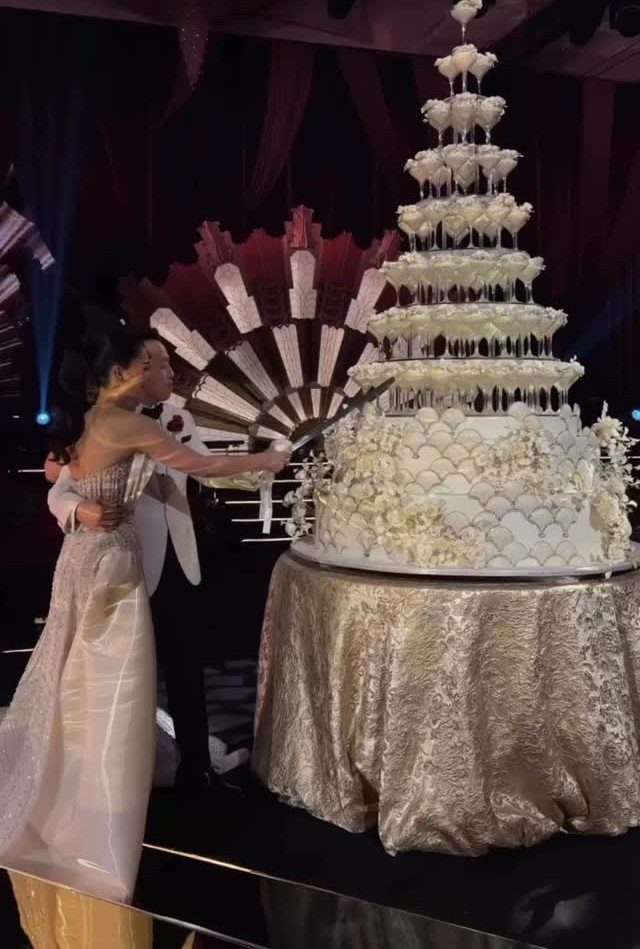 Bride and groom cutting a towering white multi-tiered wedding cake on gold tablecloth