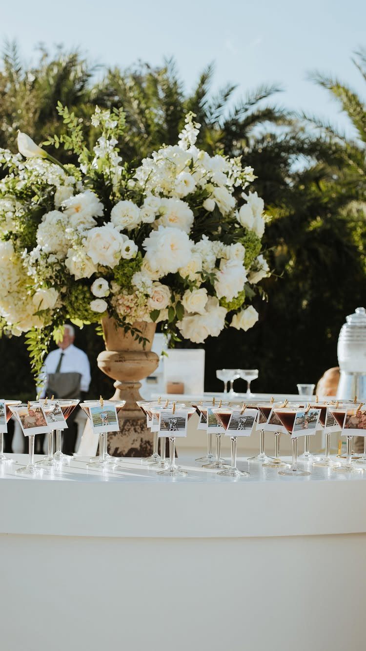 White floral centerpiece and appetizer glasses on a white table outdoors.