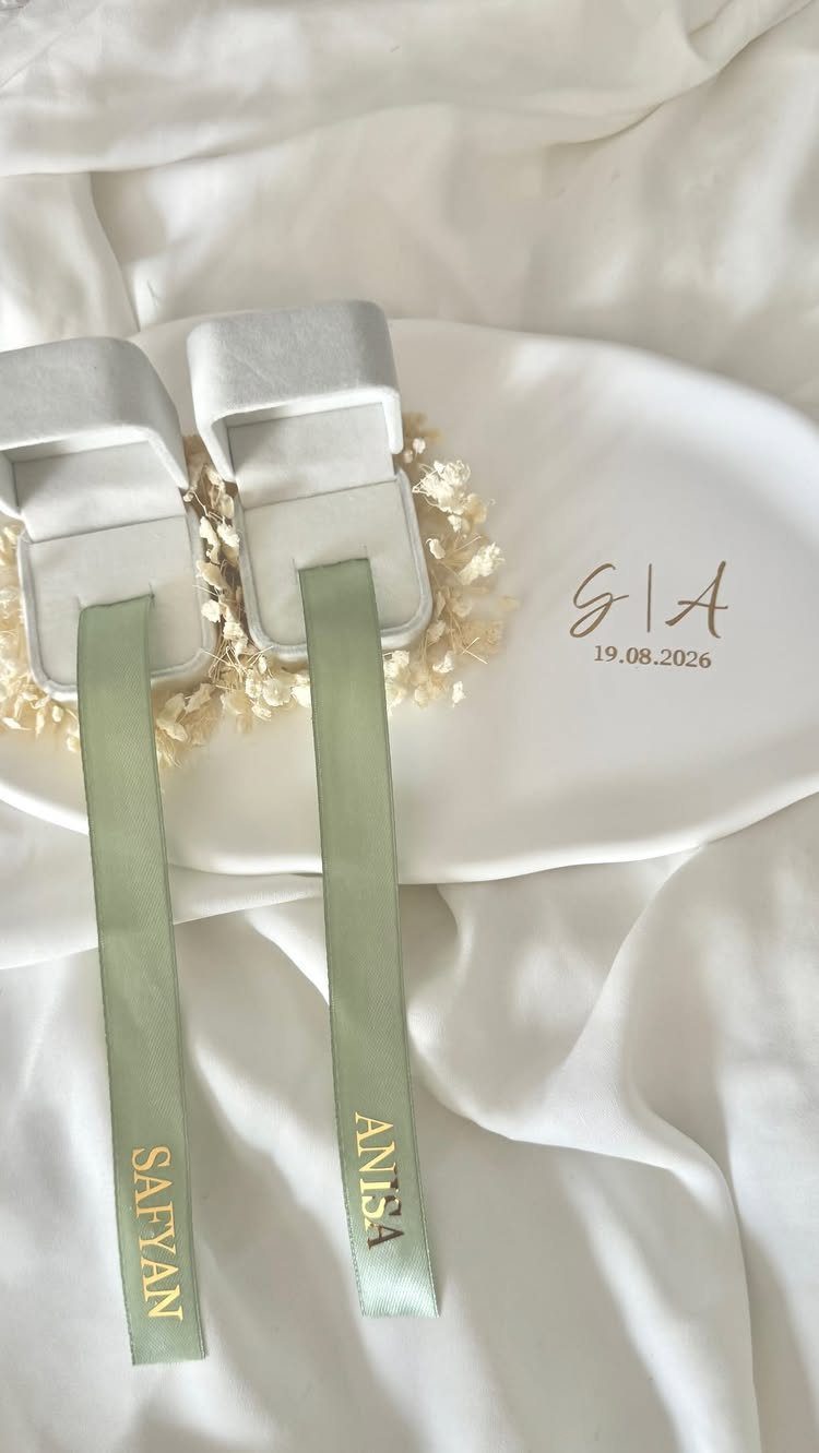 Two velvet ring boxes with personalized green ribbons on white fabric and plate.