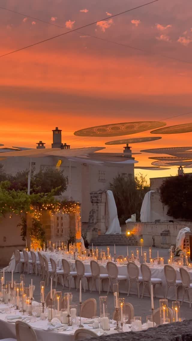 Long white dining table with candles set outdoors under a sunset sky.