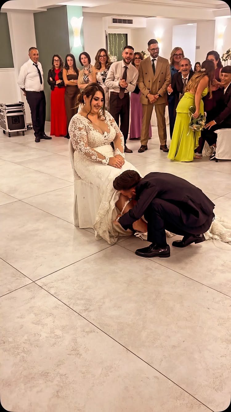 Groom kneeling to kiss the bride's foot during a wedding reception tradition.