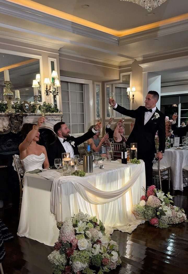 Man in tuxedo giving a toast to a bride and groom at reception.