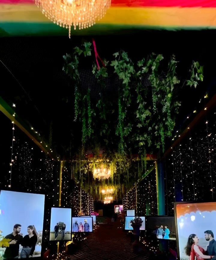 Decorated wedding walkway with hanging greenery, chandeliers, and screens showing couple photos.