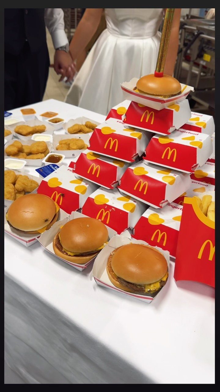 McDonald's fast food spread on a white table with a wedding couple behind.