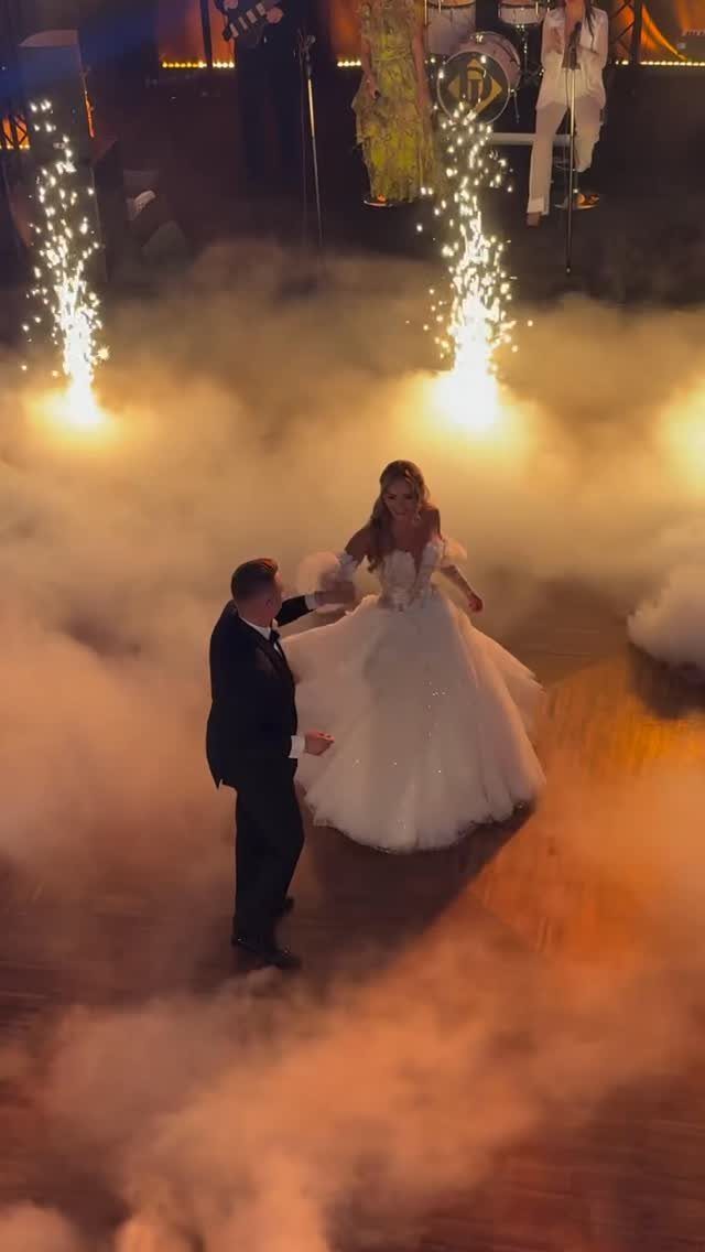 Bride and groom dancing in white fog with bright sparklers in the background.