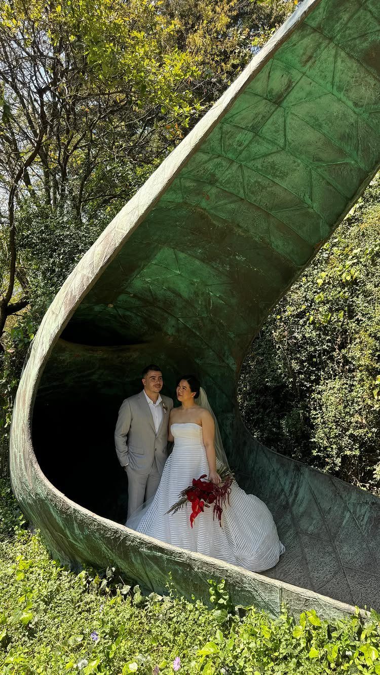 Bride and groom posing inside a large, curved green metal sculpture in a forest.
