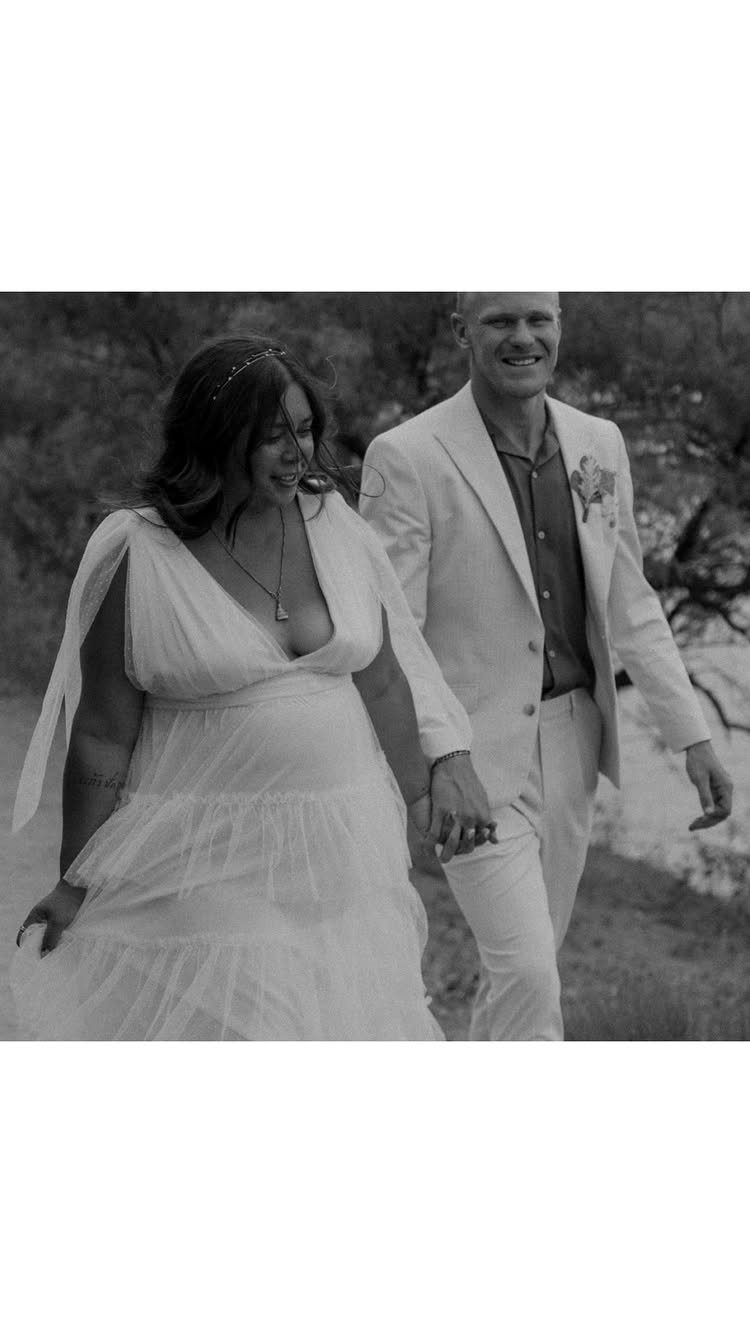 Smiling couple walking outdoors in wedding attire, captured in a candid black and white shot.