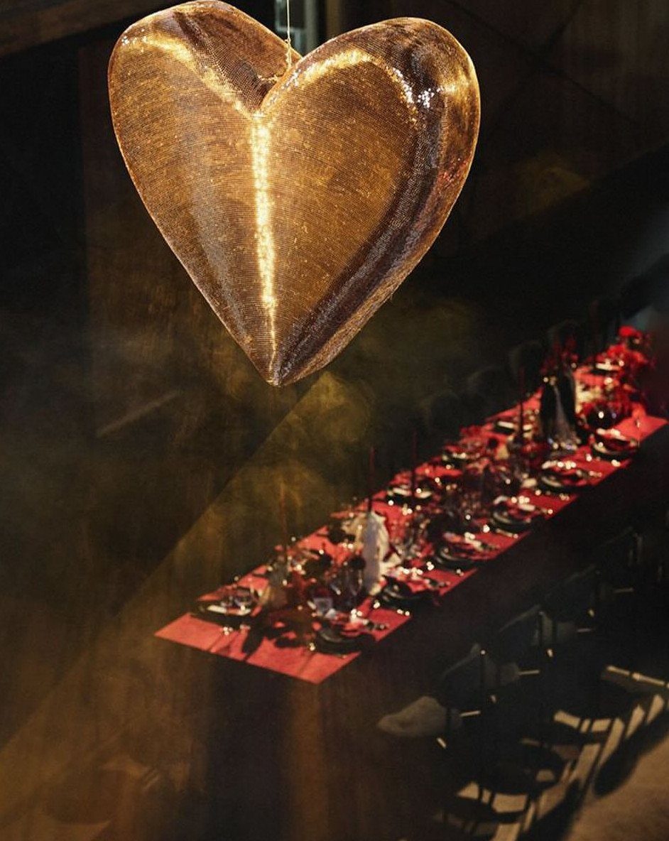 Gold heart sculpture hanging above a long dining table with red linens