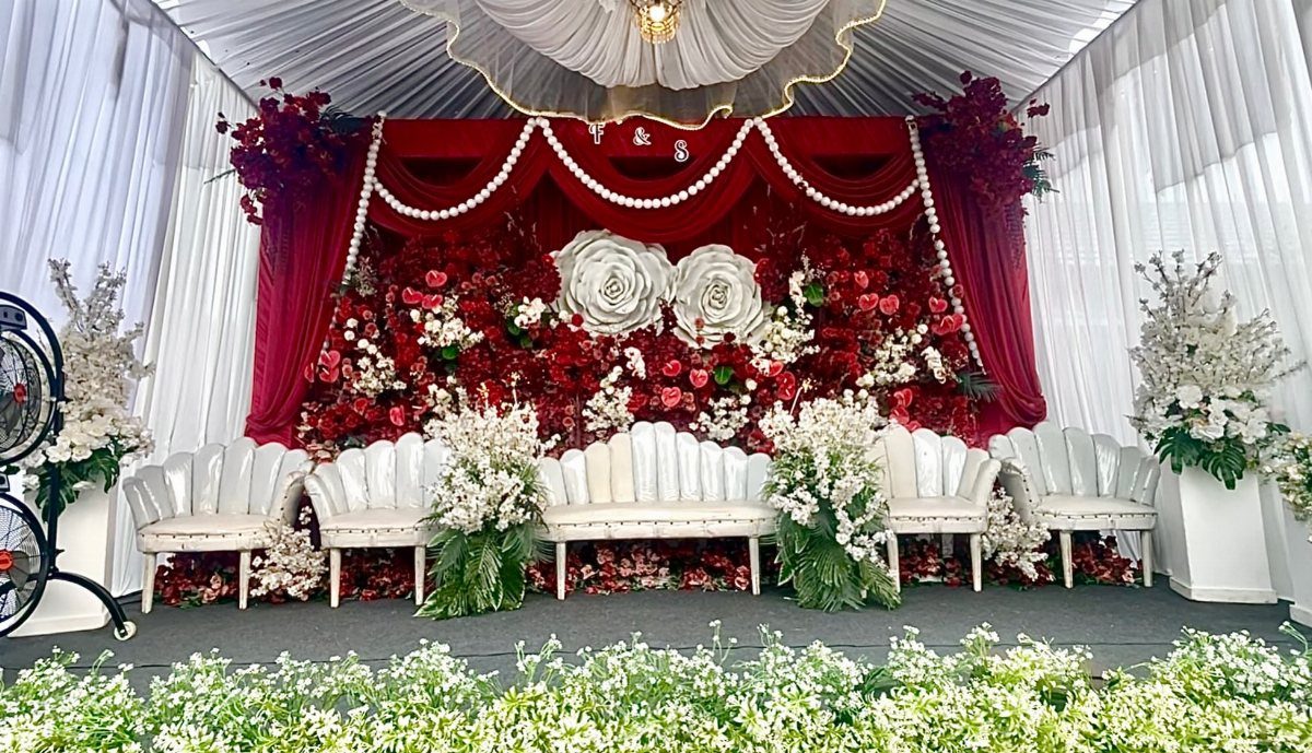 Wedding stage with red velvet backdrop, white ornate chairs, and lush floral installations.
