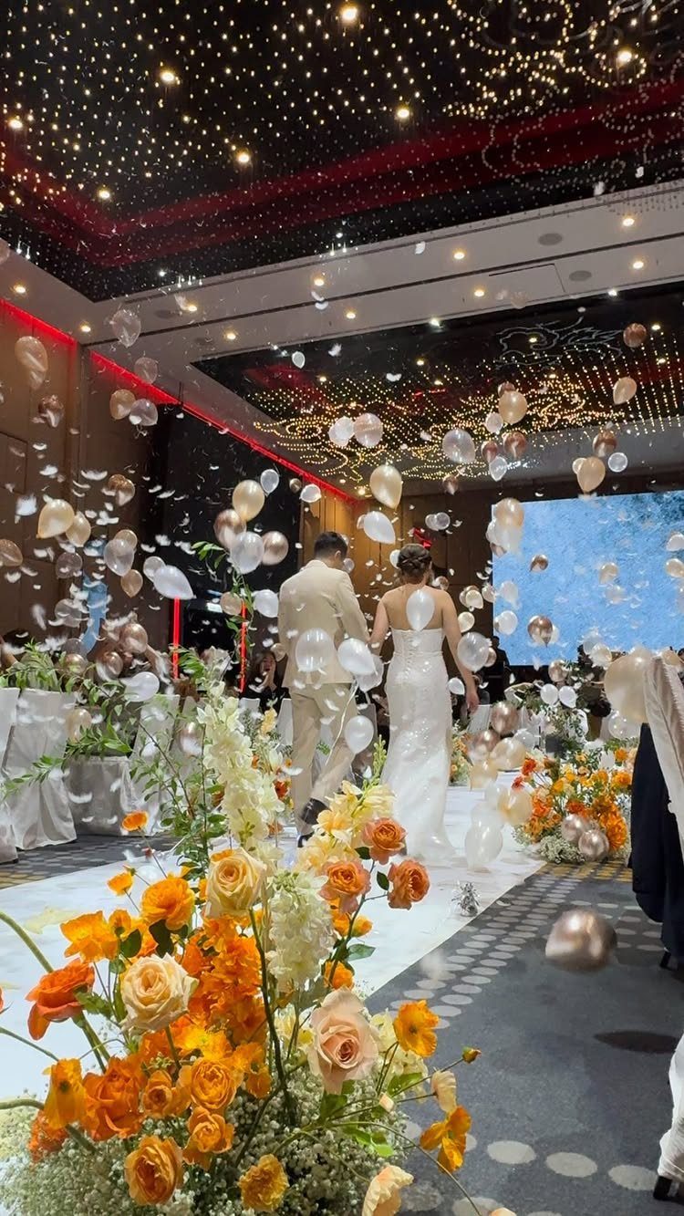Bride and groom walking through a shower of white and gold balloons at wedding.