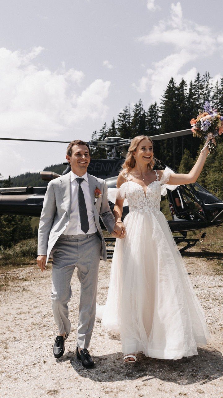Bride and groom walking away from a black helicopter in a forest setting.