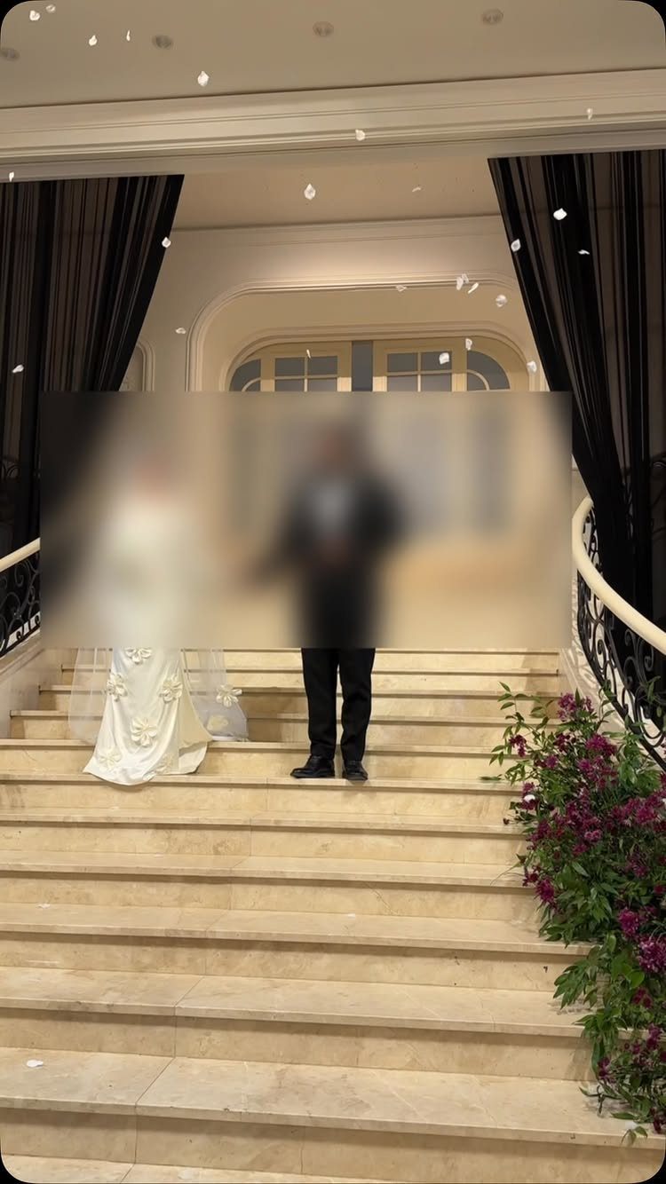 Bride and groom standing at the top of a grand marble staircase with petals.