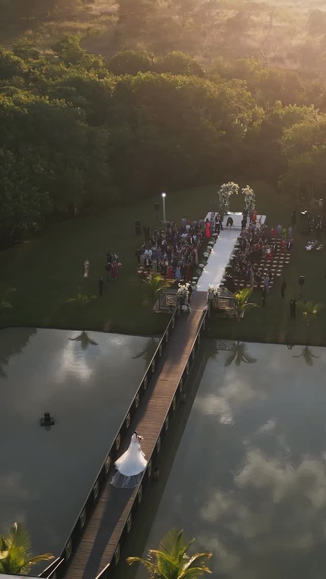 Bride in white gown walking across a wooden bridge toward outdoor wedding ceremony