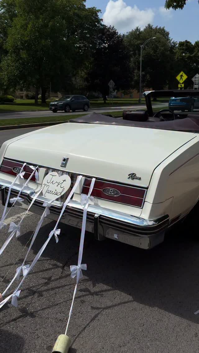 White vintage convertible car decorated with ribbons and a Just Married heart sign.