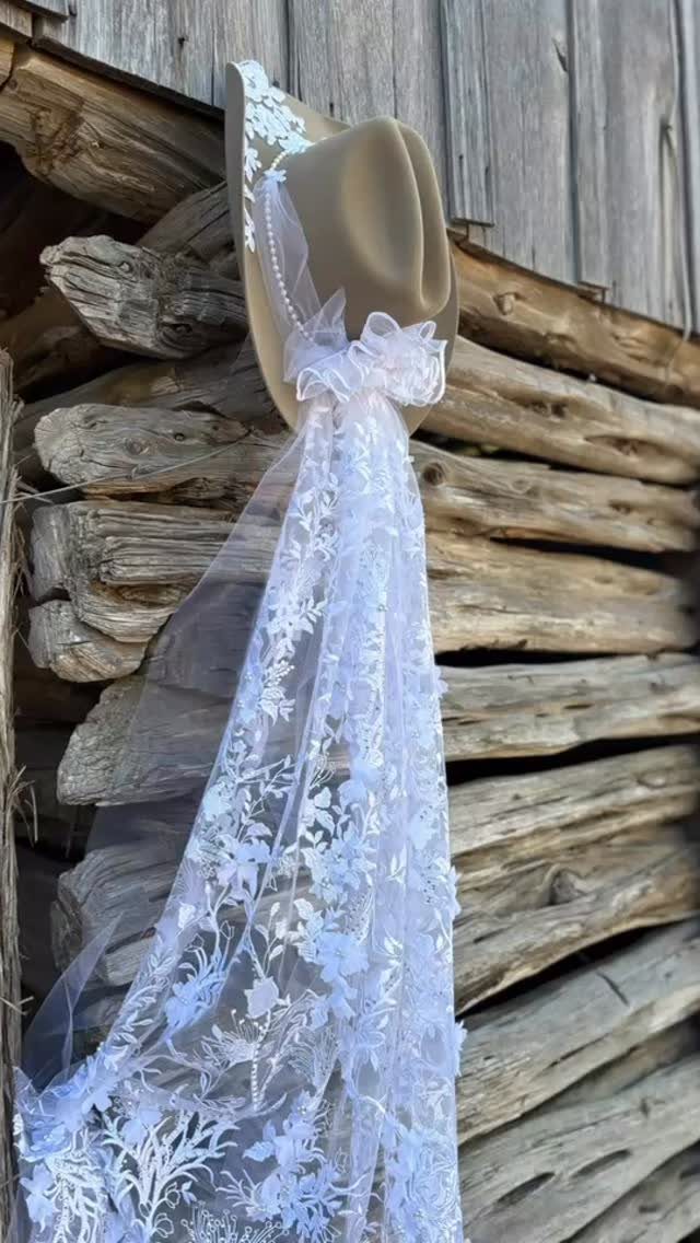 Tan cowboy hat with a white floral lace veil hanging on rustic logs