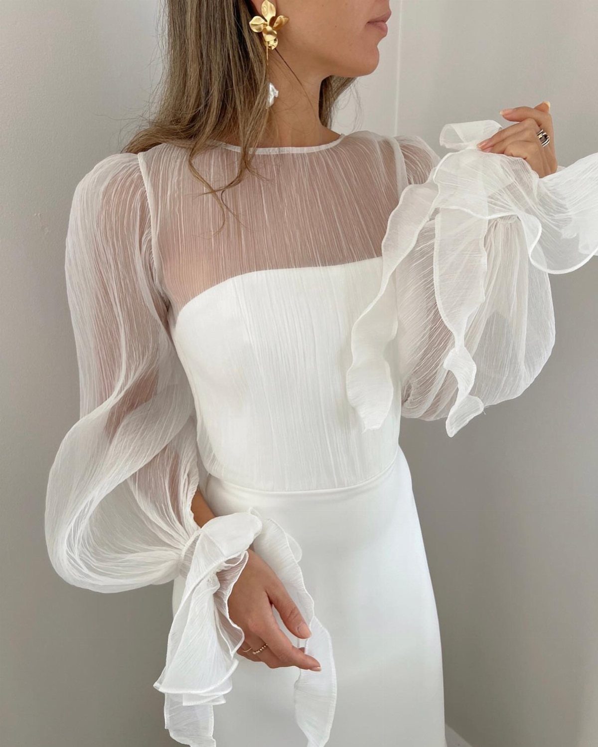 Woman wearing a white dress with voluminous, sheer ruffled puff sleeves.