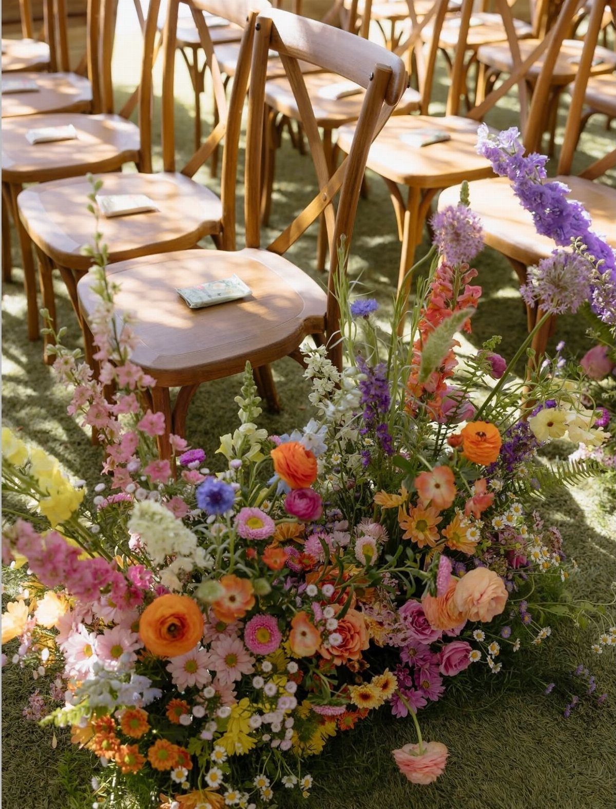 Colorful wildflower floral arrangement on grass in front of wooden wedding chairs.