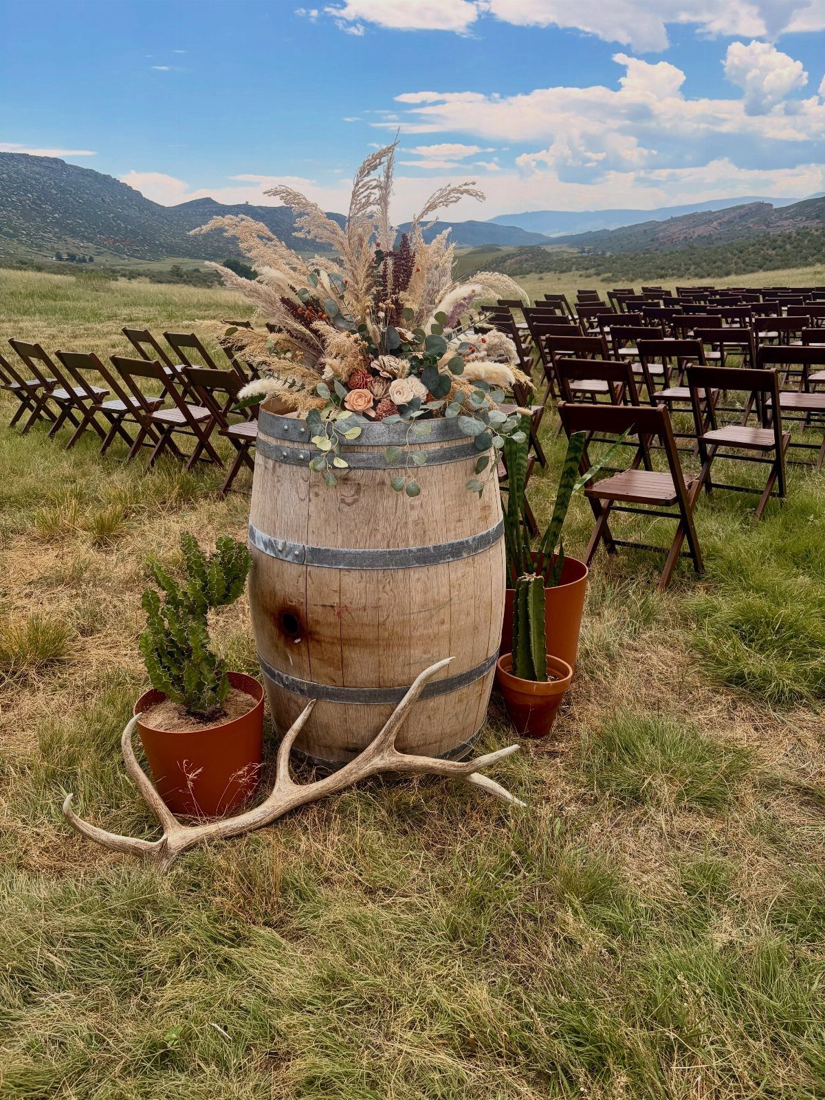 Wooden barrel with dried floral arrangement and antlers in an outdoor wedding setting