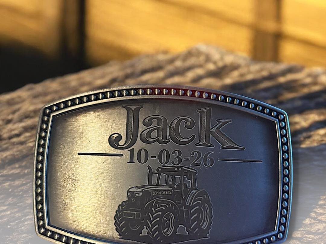 Silver metal belt buckle engraved with the name Jack, a date, and a tractor.