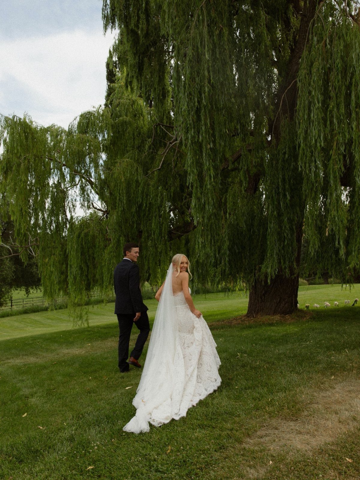Bride and groom standing on a lawn under a large weeping willow tree