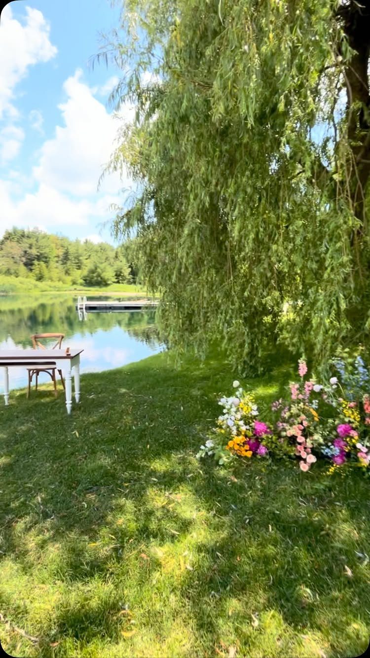 Weeping willow tree overhanging a lakeside wedding setup with white table and flowers