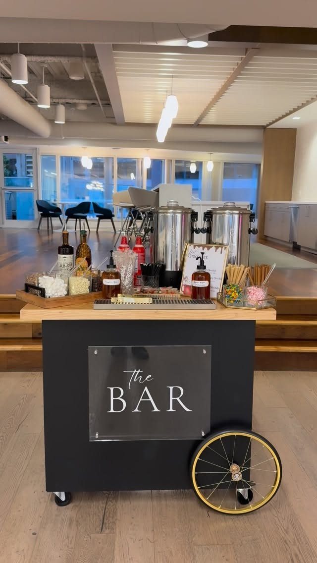 Mobile beverage bar with silver dispensers and toppings on a wooden cart.