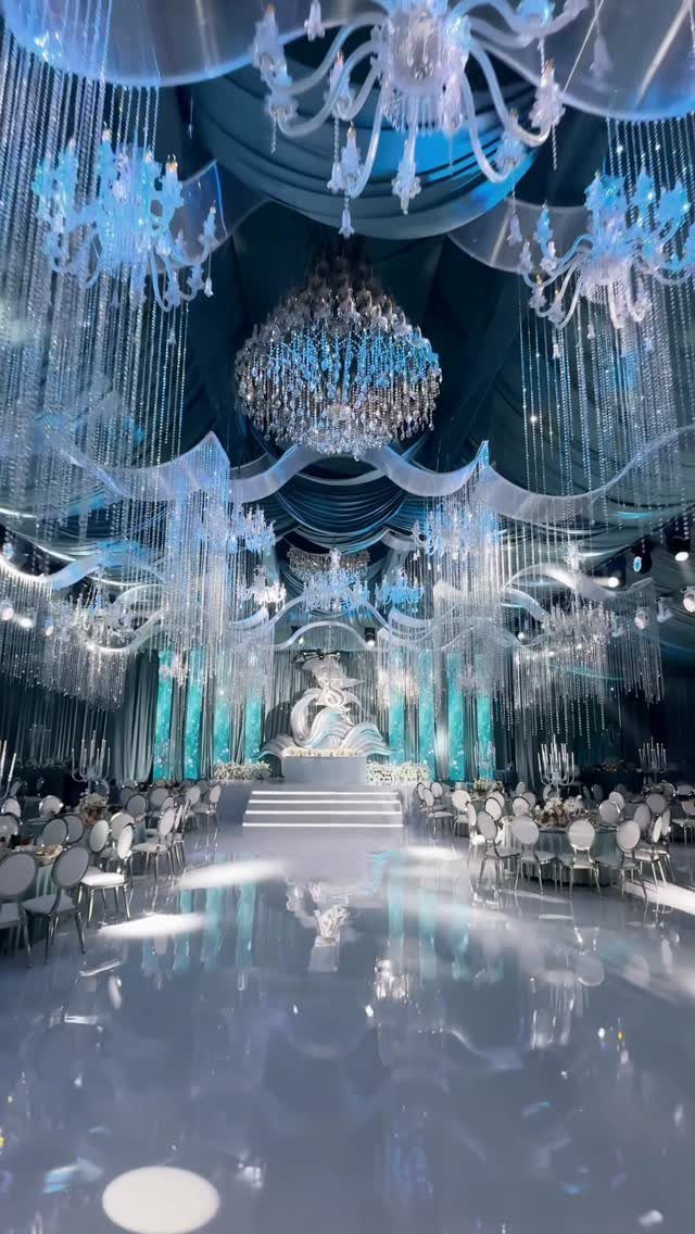 Lavish wedding reception hall with icy blue lighting and massive crystal chandeliers.