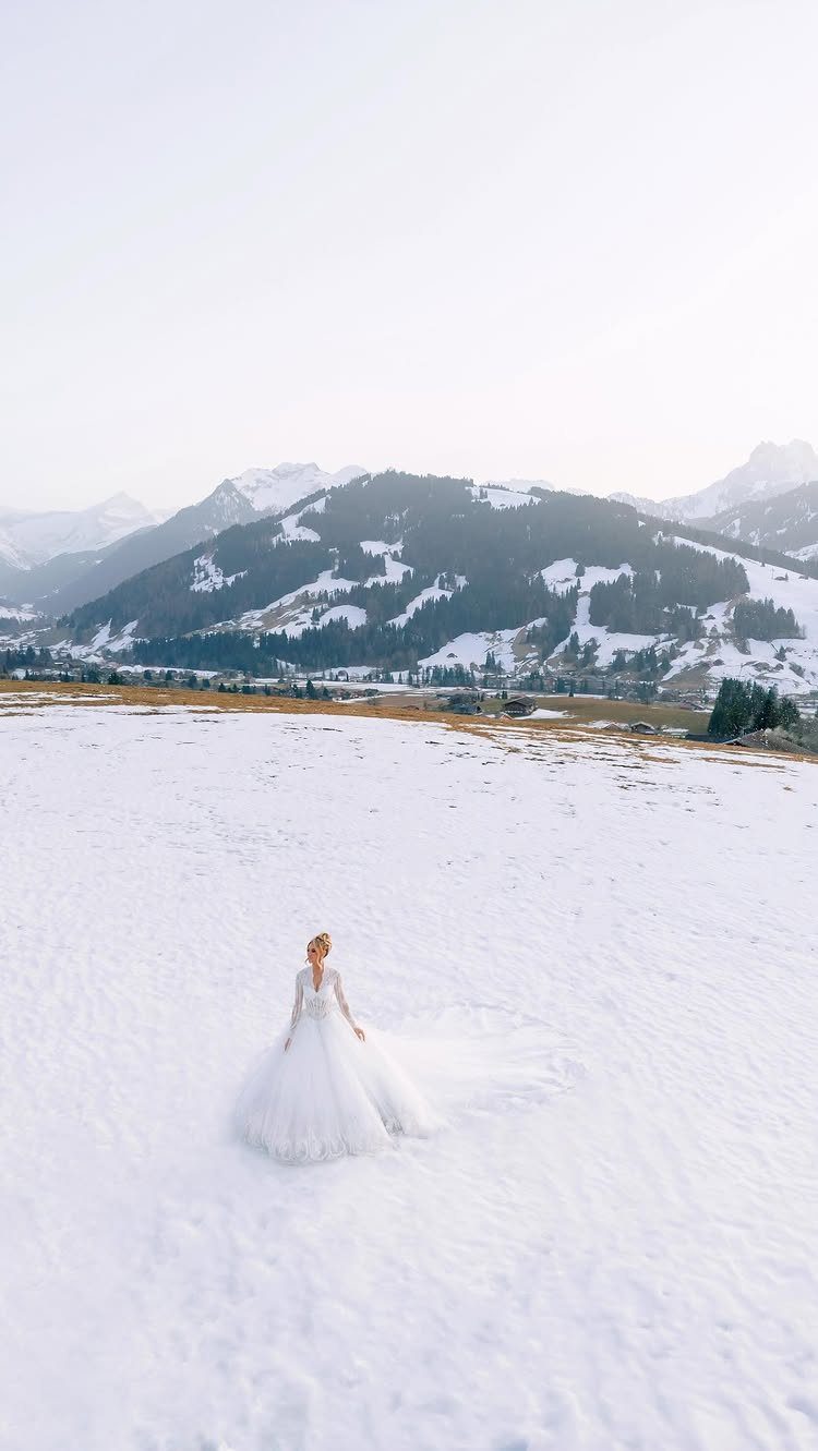 Bride in a white wedding gown standing in a snowy mountain landscape
