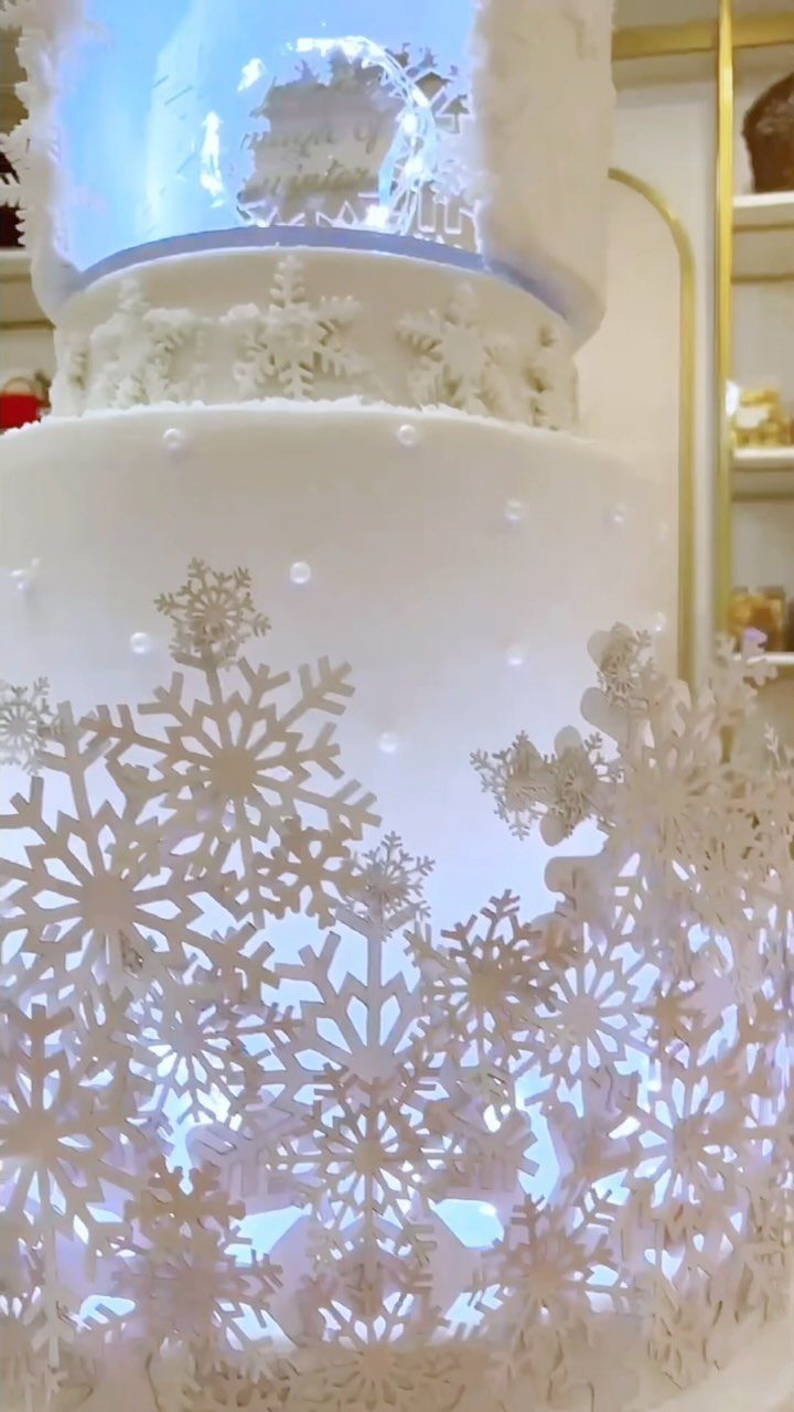 White tiered wedding cake with snowflake decorations and a glowing blue snow globe topper.