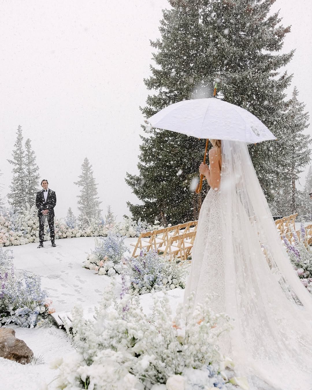 Bride with white umbrella and groom in snowy landscape with winter floral arrangements